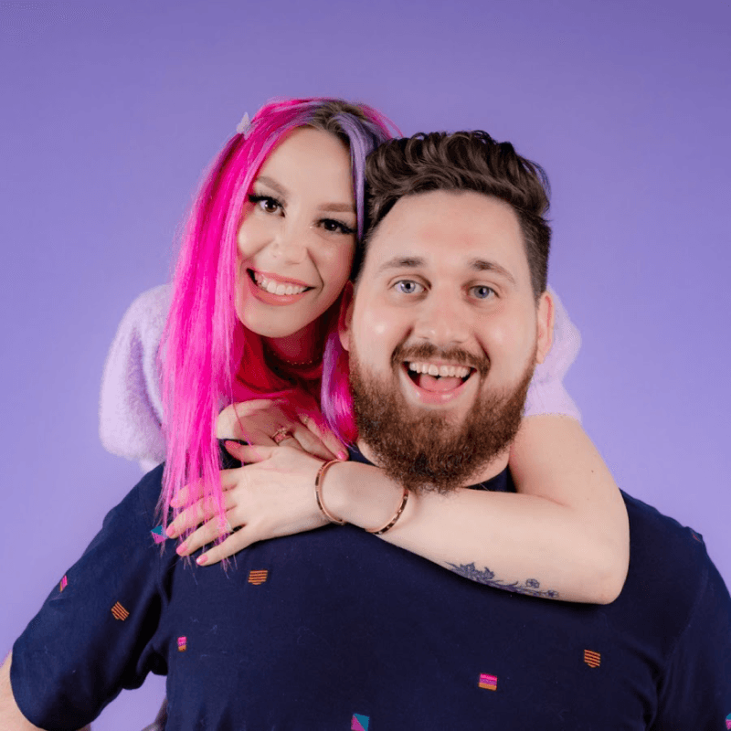 A portrait of Megan and Zach against a light purple background. Megan is behind Zach and has her arm around his shoulders.